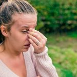 woman outdoors rubbing eyes allergies